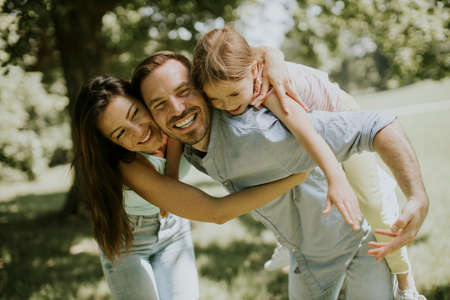 Happy young family with cute little daughter having fun in park on a sunny day