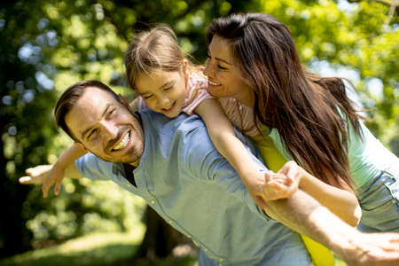 Happy young family with cute little daughter having fun in park on a sunny day