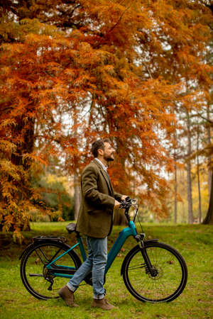 Handsome young man with electric bicycle using mobile phone in the autumn parkの写真素材