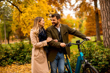 Handsome young couple in the autumn park with electrical bicycle