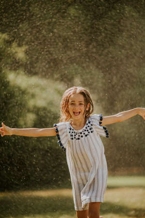 Cute little girl having fun with water under irrigation sprinklerの写真素材