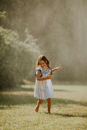 Cute little girl having fun with water under irrigation sprinklerの写真素材
