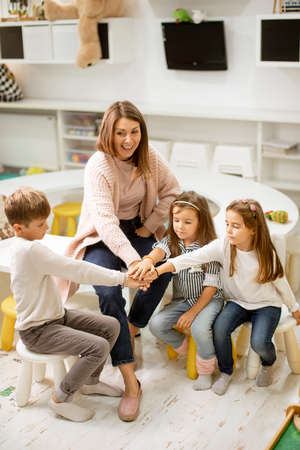 Group of cute preschool kids put hands together with their nursery teacher