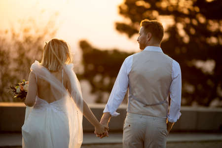 Rear view of the cute young newlywed couple walking in the parkの写真素材