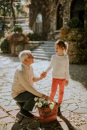 Grandfather having fun with his cute little granddaughter and holding basket full of flowersの写真素材