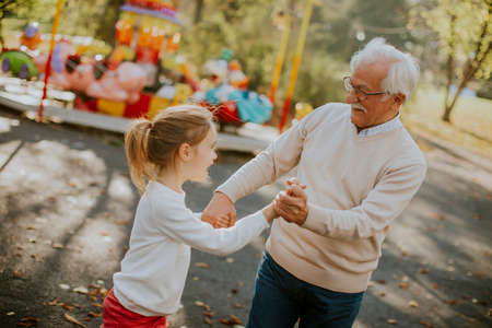Grandfather having fun with his cute little granddaughter in the amusement parkの写真素材