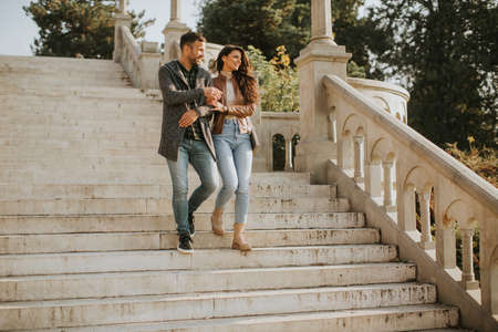 Pretty young couple smiling and talking while strolling down outdoor stairs on autumn dayの写真素材