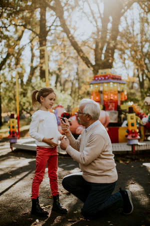 Grandfather having fun with his cute little granddaughter in the amusement parkの写真素材