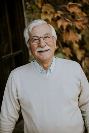 Healthy senior man standing by the window at the autumn day