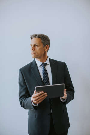 Mature business man using digital tablet by the wall in the officeの写真素材