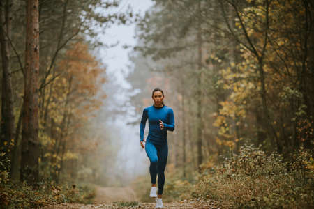 Young woman in blue track suit running toward camera on the forest trail at autumnの写真素材
