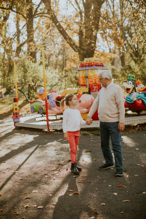 Grandfather having fun with his cute little granddaughter in the amusement parkの写真素材