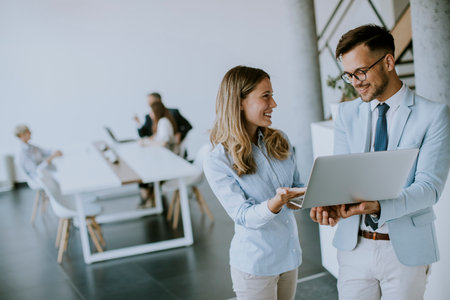 Young business couple working and discussing by laptop in the office in front of their teamの写真素材
