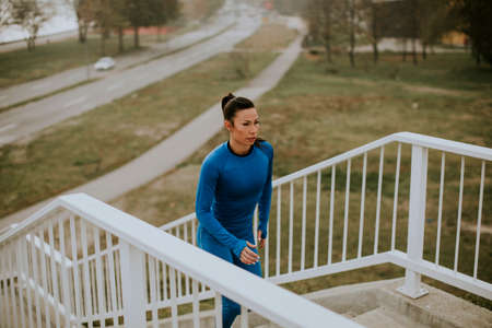 Pretty young woman in blue track suit running on the outdoor stairs at autumn morning