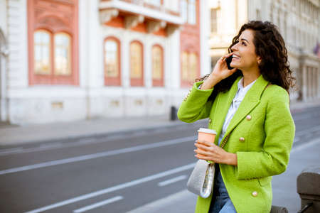 Pretty young woman using smartphone on the street and holding takeaway coffeeの写真素材