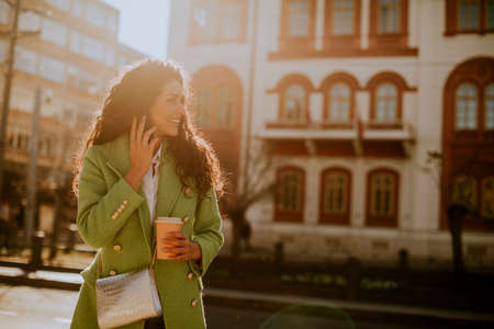 Pretty young woman using smartphone on the street and holding takeaway coffee