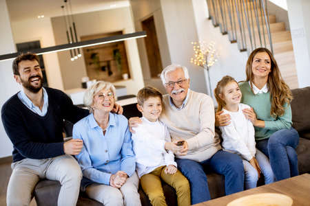 Multi generation family sitting together on the sofa at modern home and watching TVの写真素材
