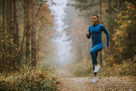 Young  woman running having exercise on the forest trail at autumnの写真素材