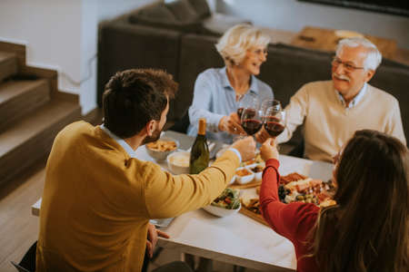 Happy family having a dinner with red wine at homeの写真素材
