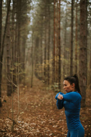Pretty young woman in blue track suit stretching before workout in the autumn forestの写真素材