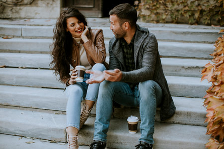 Handsome young couple sitting on outdoor stairs on a autumn day and using mobile phoneの写真素材