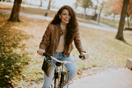 Pretty young woman riding bicycle on autumn dayの写真素材