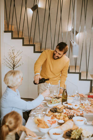 Handsome young man poring red wine to his mother for testing during at homeの写真素材
