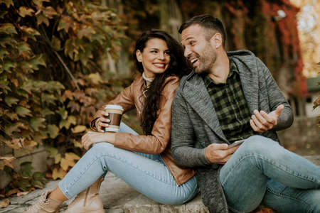 Handsome young couple sitting on outdoor stairs on a autumn day and using mobile phoneの写真素材