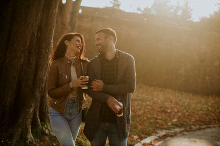 Handsome young couple walking in autumn park with coffee to go cups in handsの写真素材