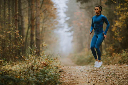 Young woman in blue track suit taking high jump on the forest trail at autumnの写真素材