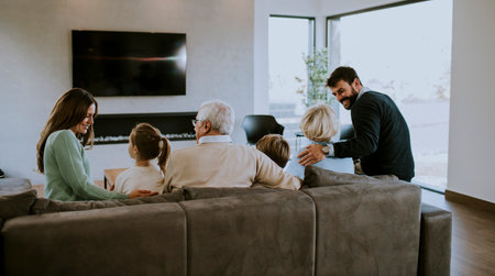 Multi generation family sitting together on the sofa at modern apartment and watching TVの写真素材