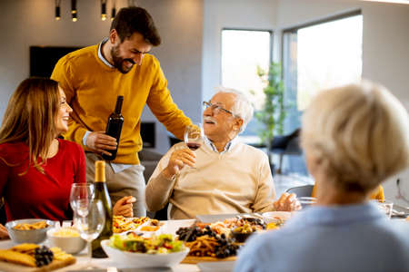 Handsome young man poring red wine to his father for testing during at home
