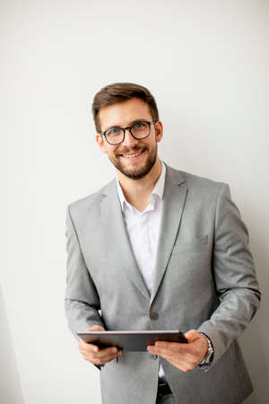 Handsome young modern businessman using digital tablet by the wall in the office