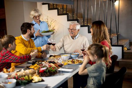 Happy family having a dinner with red wine at homeの写真素材