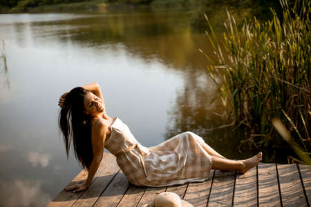 Young woman relaxing on the wooden pier at the calm lake on a hot summer dayの写真素材