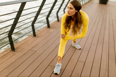 Pretty young woman having stretching exercise on the riverside pierの写真素材