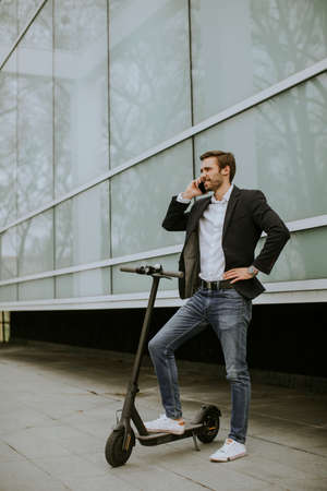 Handsome young businessman using mobile phone  on electric scooter