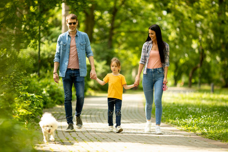 Happy young family with cute bichon dog in the parkの写真素材
