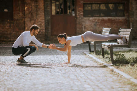 Pretty young woman doing puhsups with personal trainer on the streetの写真素材