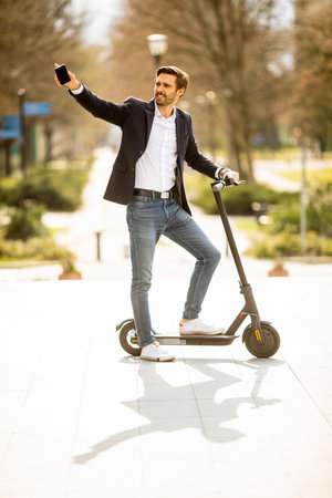 Handsome young businessman using mobile phone  on electric scooterの写真素材