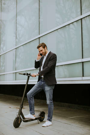 Handsome young businessman using mobile phone  on electric scooter