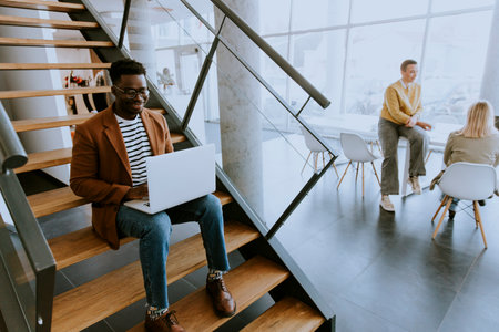 Handsome young African American business man working on laptop computer while sitting on a office stairsの写真素材