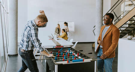 Young handsome casual multiethnic business people playing table football and relaxing at officeの写真素材