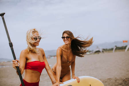 Two pretty young women with paddle board on the beach on a summer dayの写真素材