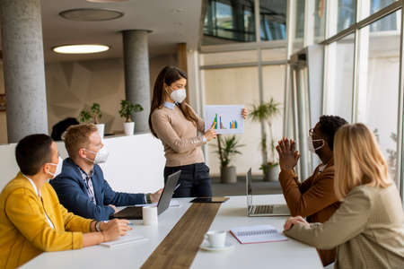 Group of young multiethnic business people working together with facial protective masks and...