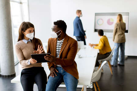 Handsome young African American business man and cute business woman working on digital tablet while wearing a facial protective masksの写真素材