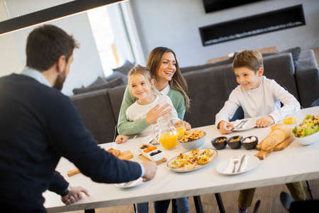 Young happy family talking while having breakfast at dining table at apartmentの写真素材