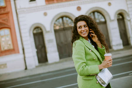 Pretty young woman using smartphone on the street and holding takeaway coffeeの写真素材