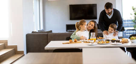 Young happy family talking while having breakfast at dining table at apartmentの写真素材