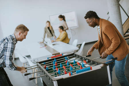 Young handsome casual multiethnic business people playing table football and relaxing at office